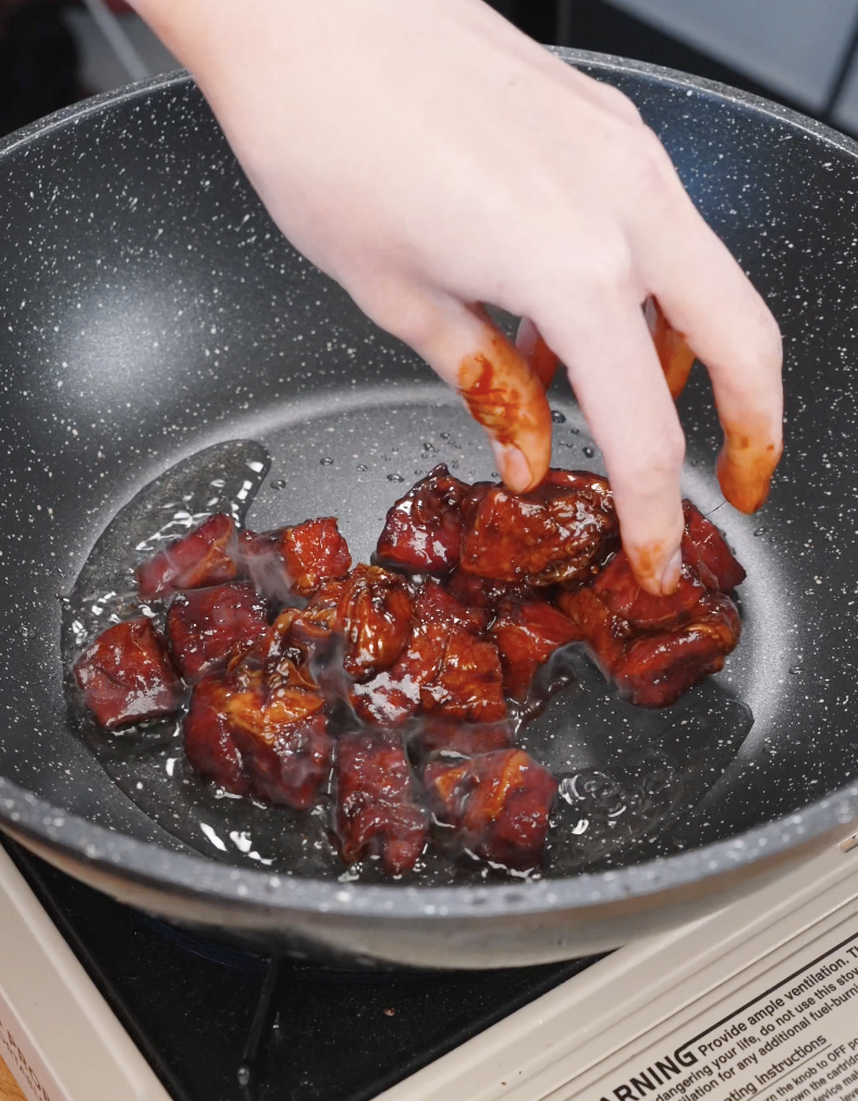 Hand placing marinated steak cubes into a hot pan, beginning the searing process for Korean BBQ steak.