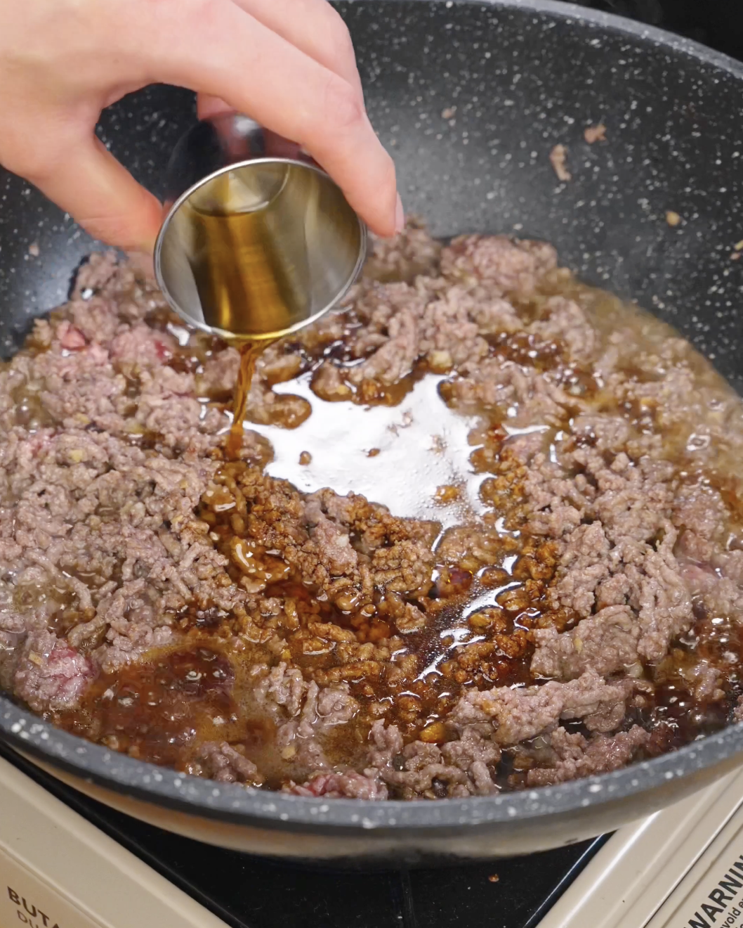 Soy sauce and seasonings being poured into ground beef while cooking bulgogi ground beef.