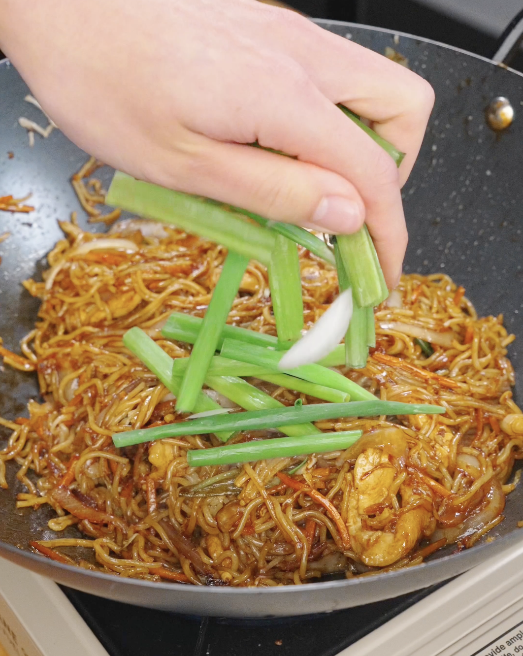 Fresh scallion greens being added to chicken chow mein in a pan, finishing the dish with color and freshness.