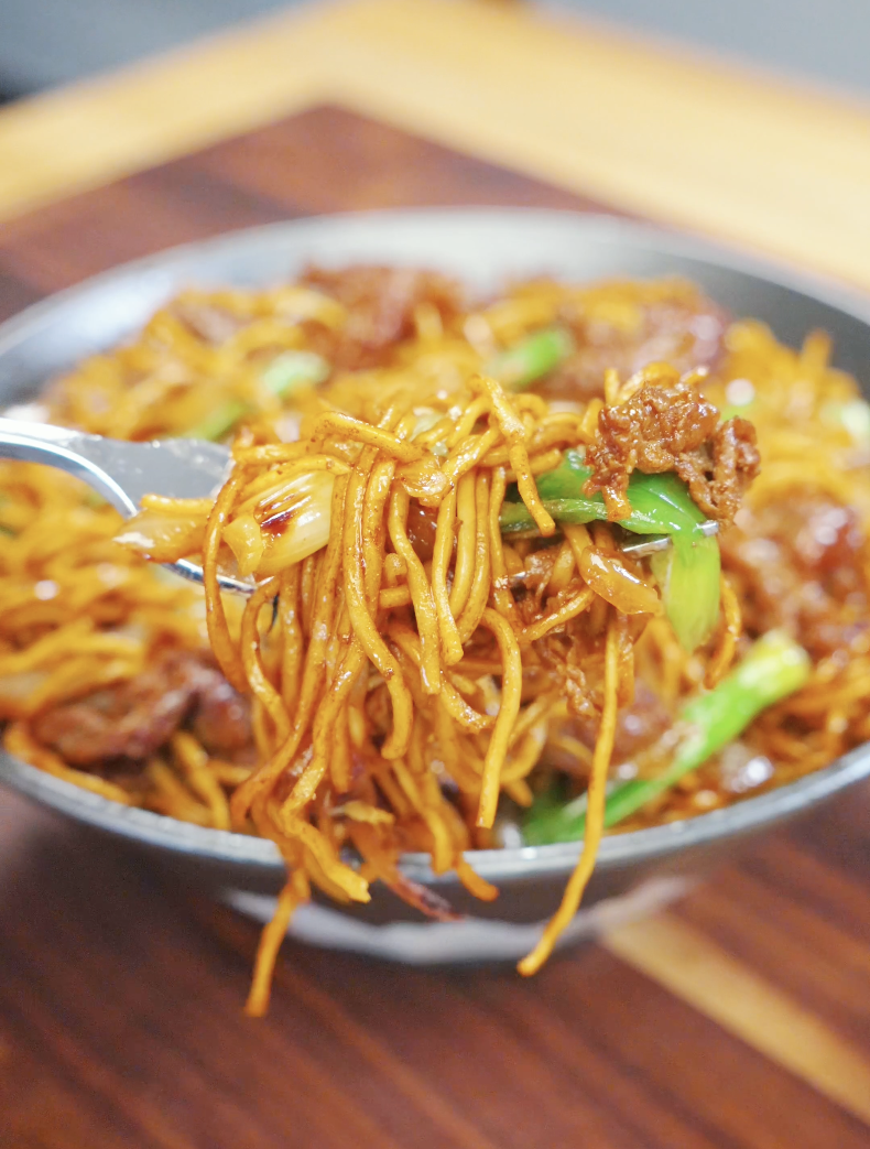 Fork lifting saucy chow mein noodles with tender beef, scallions, and onions coated in a glossy soy-based sauce in this Beef Chow Mein Recipe.