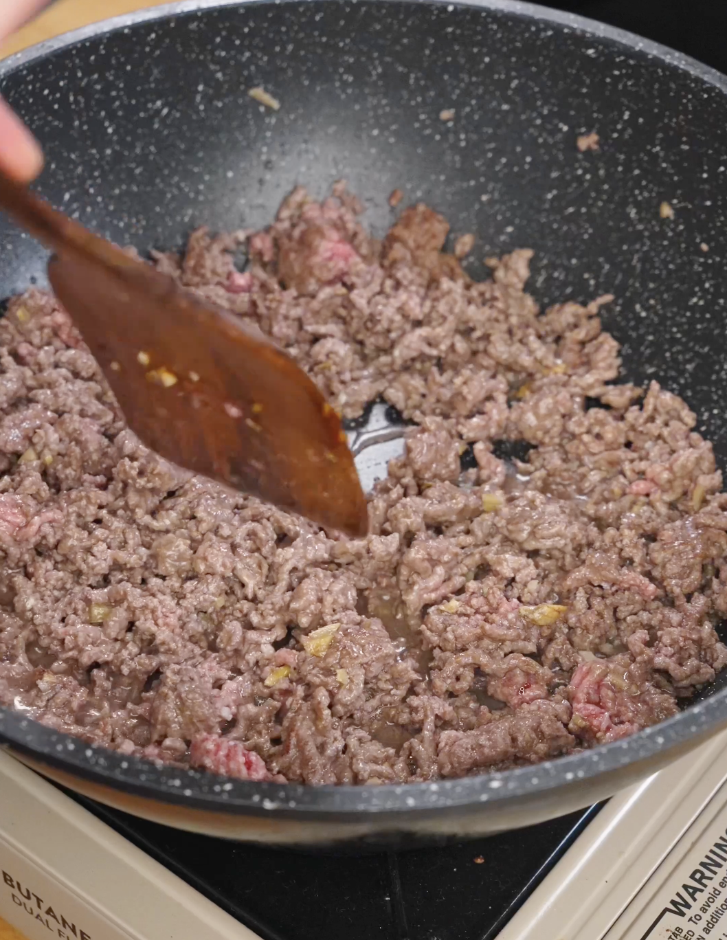 Ground beef cooking in a pan as it browns and releases juices for bulgogi ground beef.