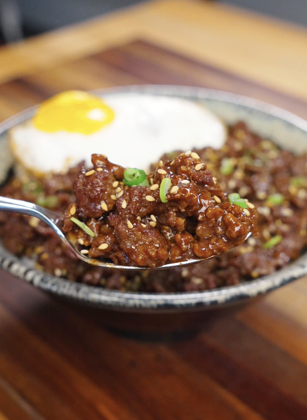 Spoon lifting a bite of bulgogi ground beef over rice coated in a glossy soy garlic sauce.