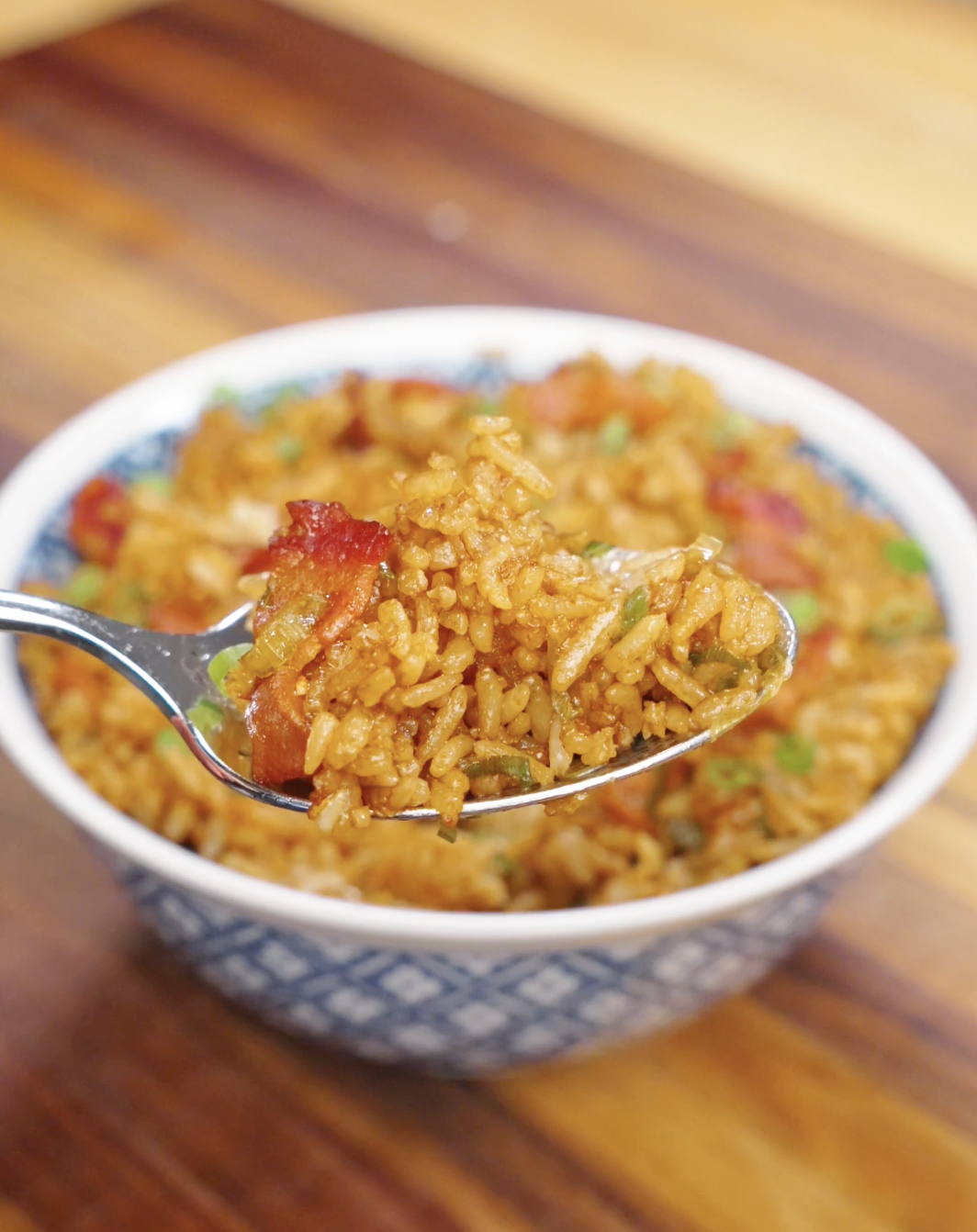 Spoon lifting garlic bacon fried rice with crispy bacon and scallions coated in a savory sauce.