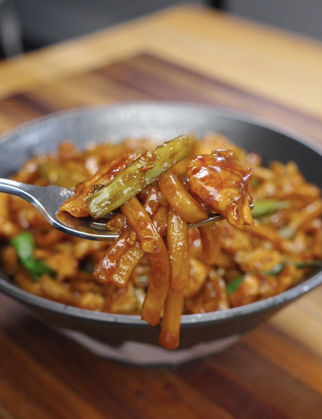 Fork lifting garlic chicken noodles with tender chicken and scallions coated in savory sauce.