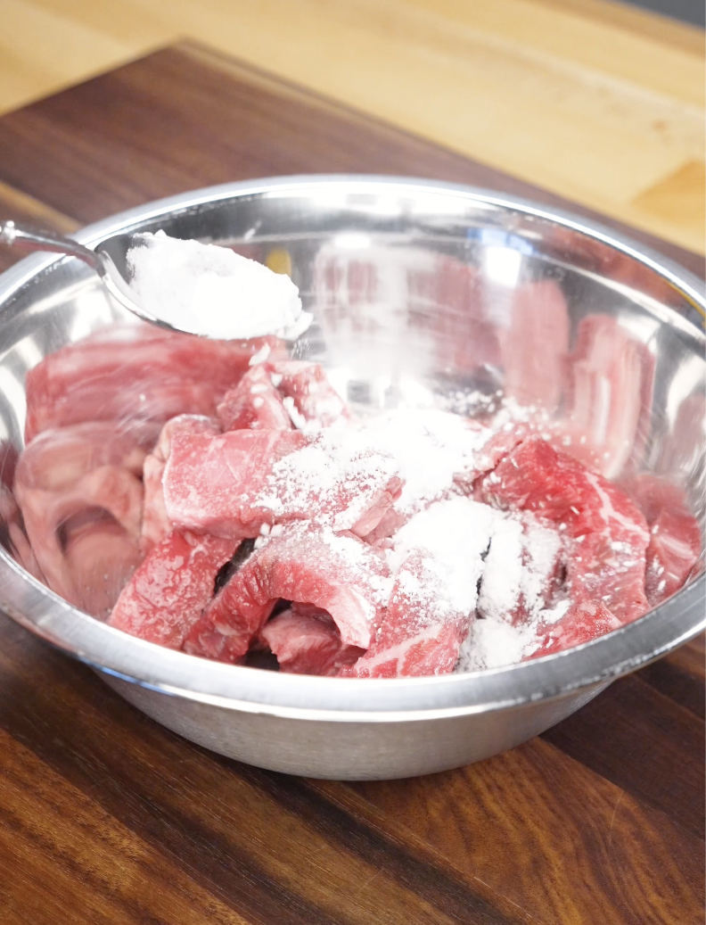 Thinly sliced sirloin beef being dusted with cornstarch in a metal bowl, a key step in the Mongolian Beef Recipe to create tender texture and better searing.