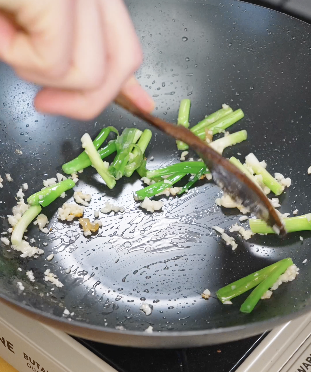 Garlic and scallion whites saut&eacute;ing in oil to build flavor for garlic chicken noodles.