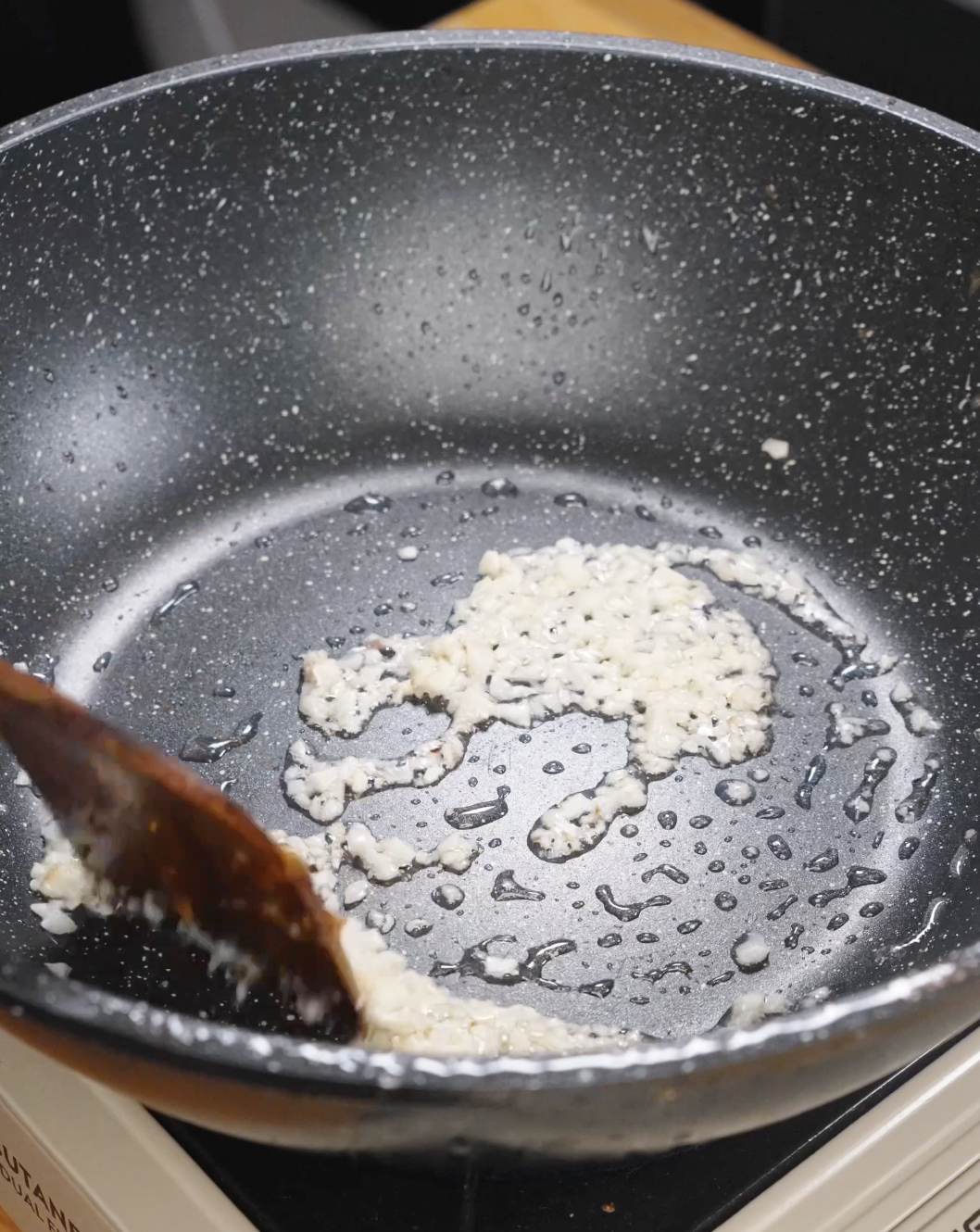 Minced garlic sizzling in oil in a nonstick pan, releasing aroma as the flavor base for garlic beef fried rice develops.