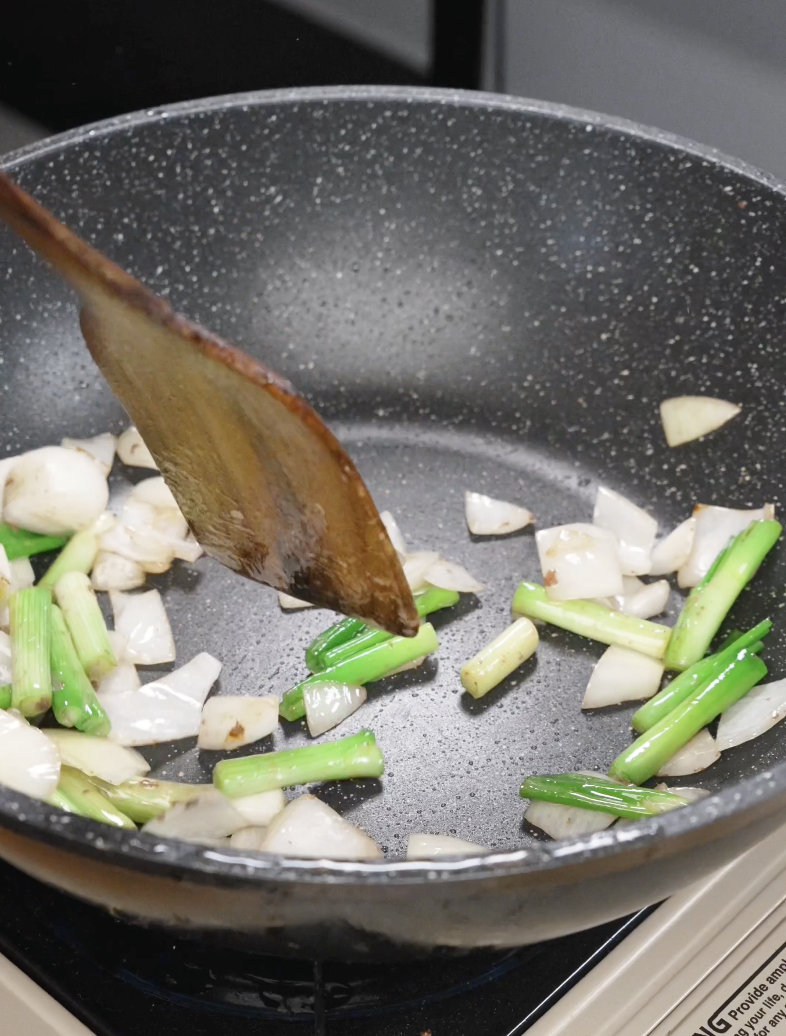 Onions and scallion whites saut&eacute;ing in a pan with a wooden spatula, building flavor for the Mongolian Beef Recipe.