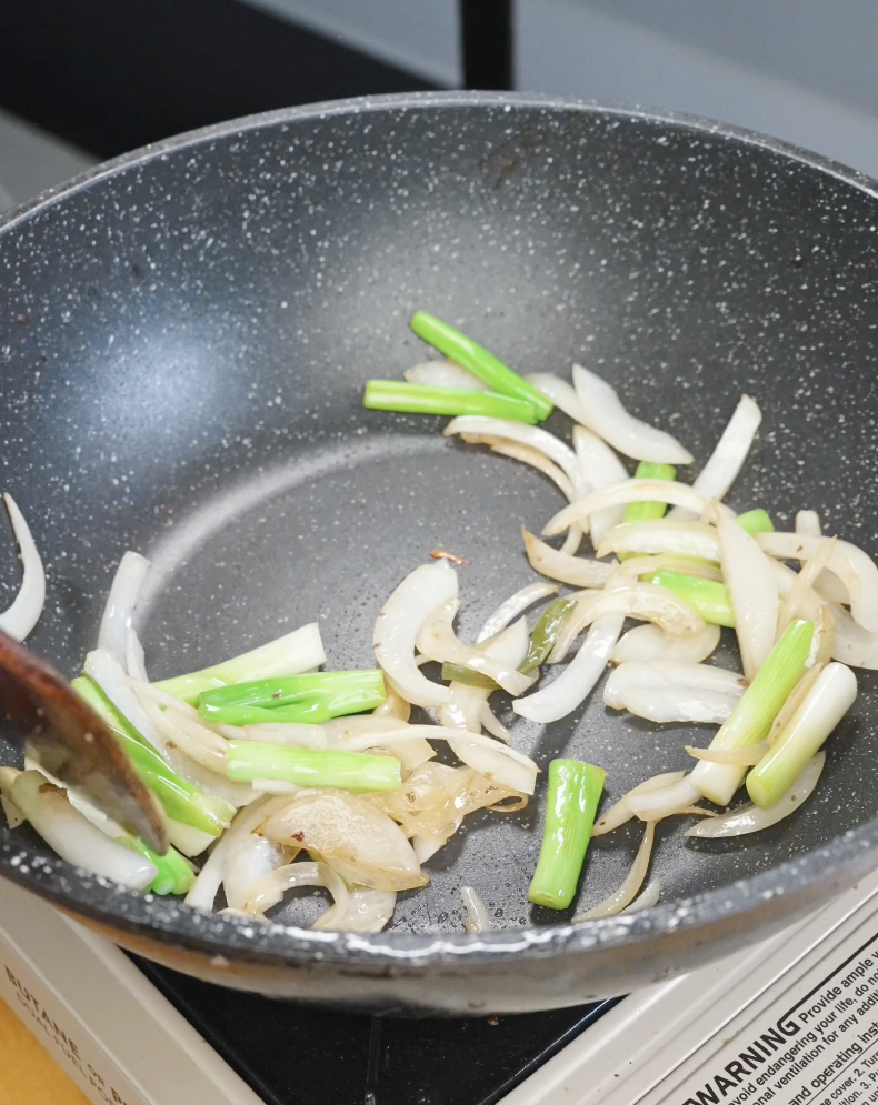 Onions and scallion whites saut&eacute;ing in a pan until softened and lightly caramelized in the Beef Chow Mein Recipe.