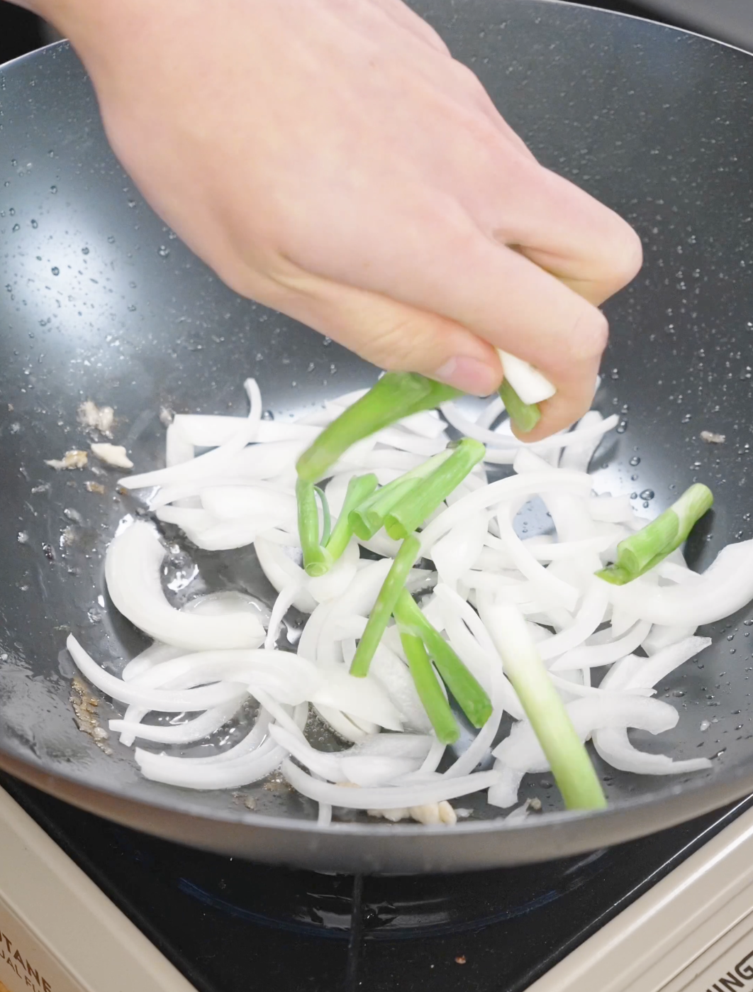Sliced onions and scallion whites being saut&eacute;ed in a pan, building the aromatic base for chicken chow mein.