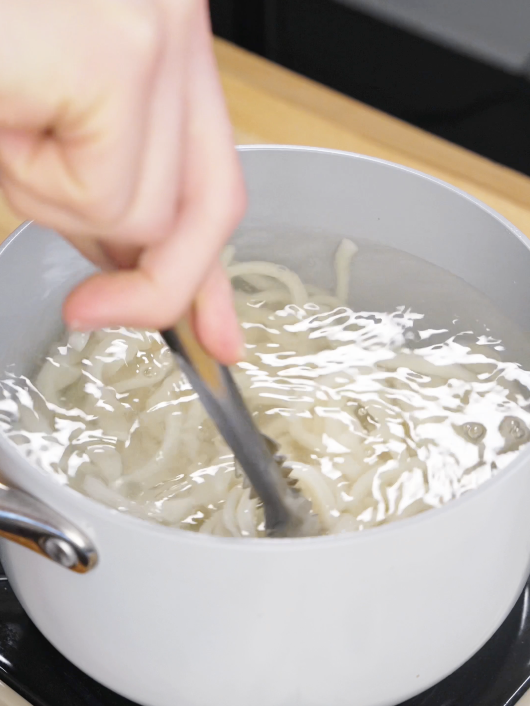 Udon noodles boiling in water in a pot before being used for garlic chicken noodles.