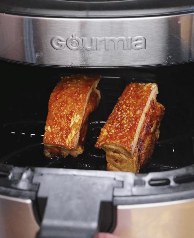 Golden blistered pork belly with crispy crackling skin inside an air fryer basket during cooking for the Vietnamese Crispy Pork Belly Recipe.