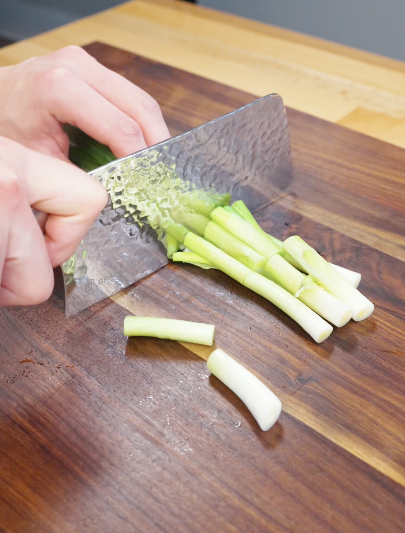 Hand slicing scallions into short segments on a wooden cutting board for stir fry preparation in the Beef Chow Mein Recipe.