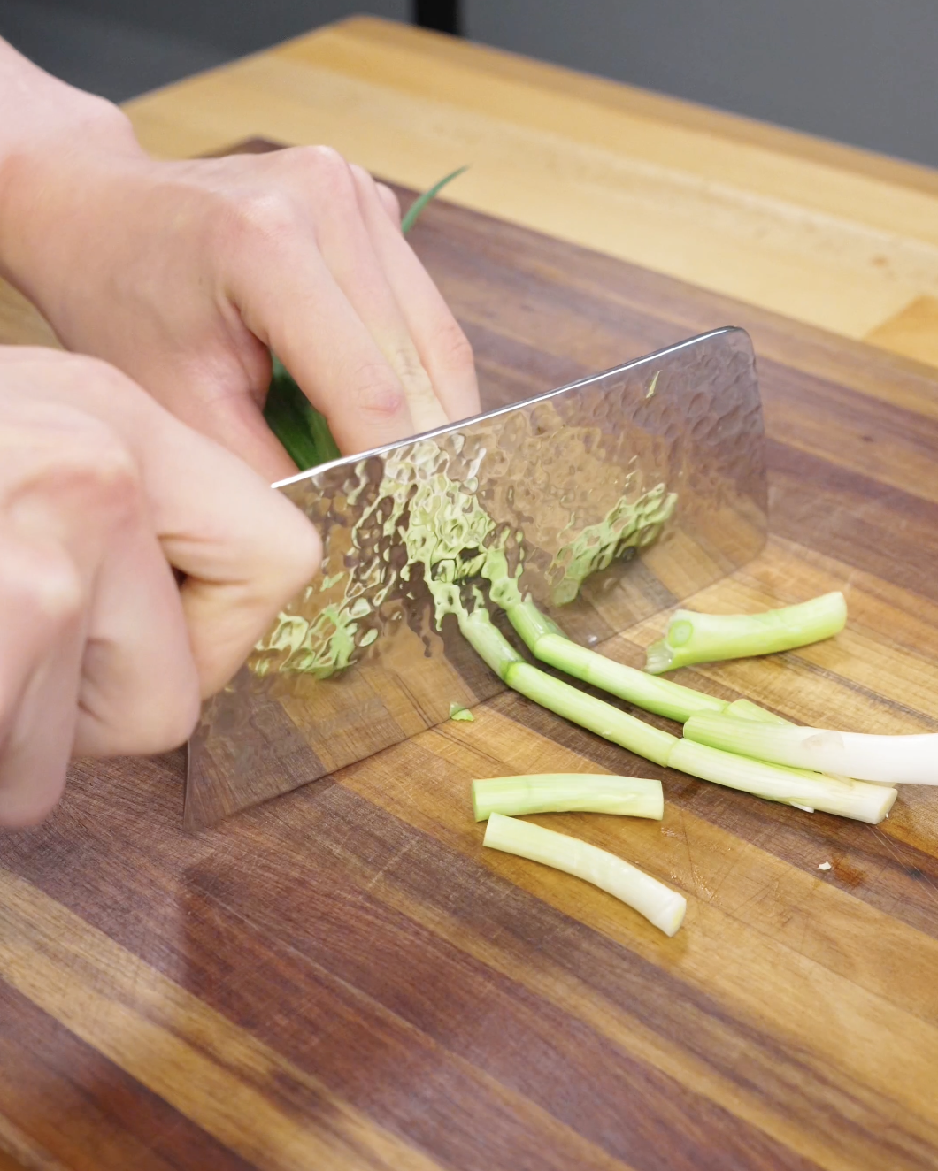 Knife slicing scallions into segments on a cutting board for garlic chicken noodles preparation.