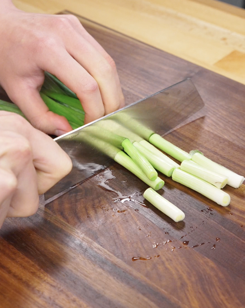 Fresh scallions being sliced into half-inch pieces on a wooden cutting board, prepping aromatics for the Mongolian Beef Recipe.
