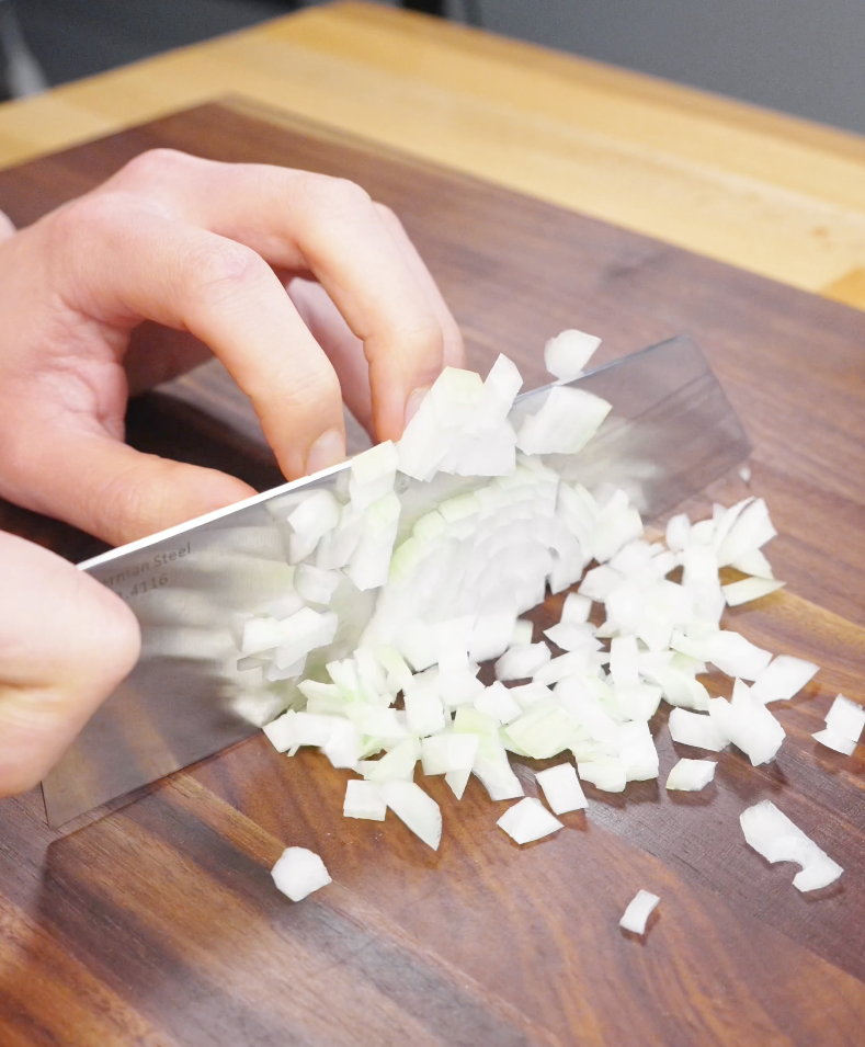 Onion being finely diced on a wooden cutting board, preparing aromatics for chicken fried rice.