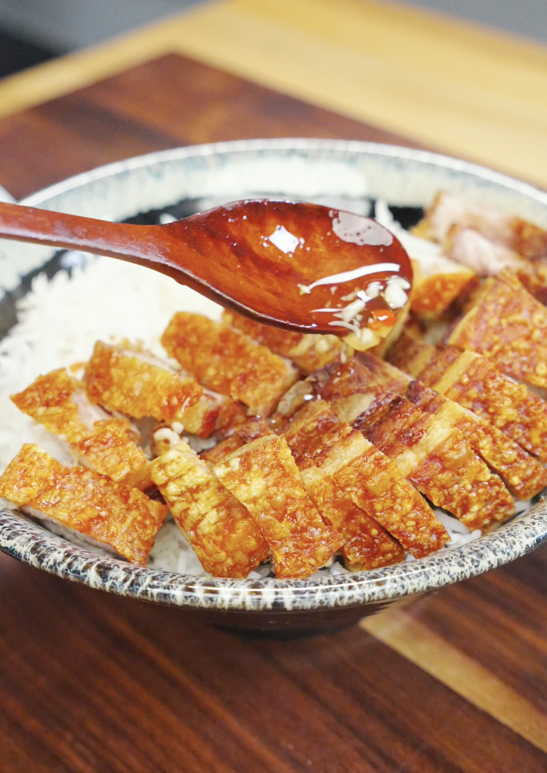 Spoon drizzling fish sauce dressing over sliced crispy pork belly on rice, highlighting glossy sauce and texture in the Vietnamese Crispy Pork Belly Recipe.