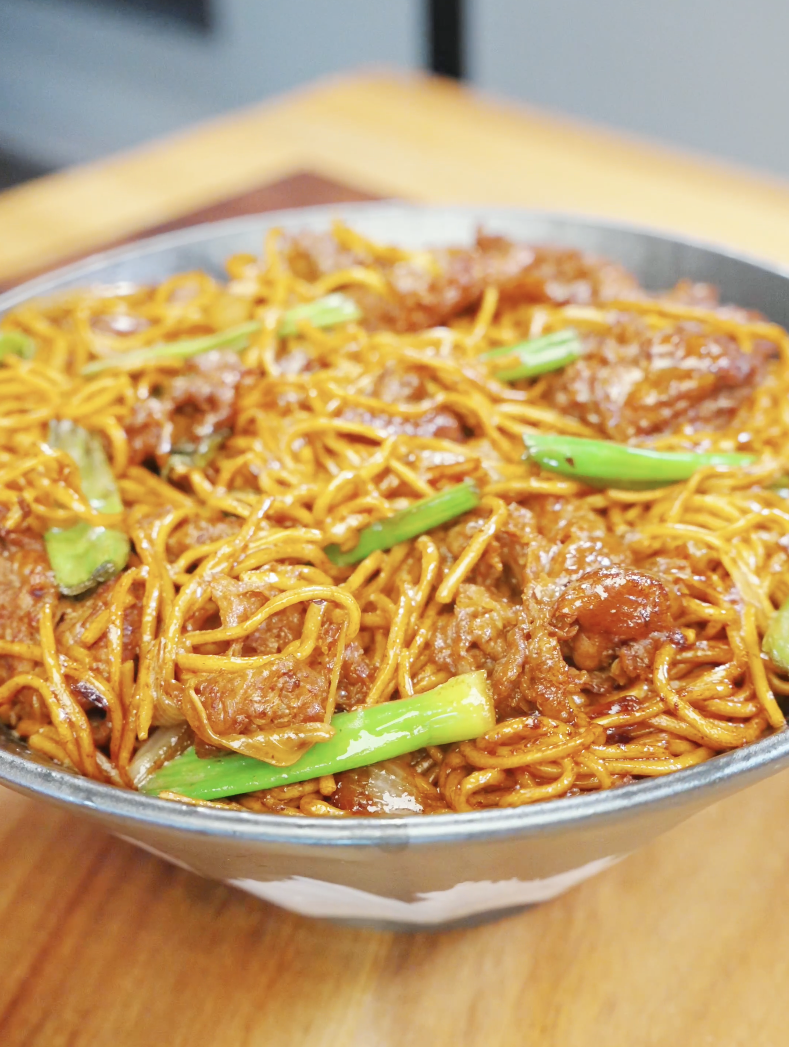 Bowl of beef chow mein with noodles, onions, and scallions tossed in a rich glossy sauce in the Beef Chow Mein Recipe.