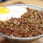 Bowl of bulgogi ground beef served over rice with sesame seeds scallions and a fried egg.