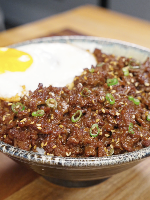 Bowl of bulgogi ground beef served over rice with sesame seeds scallions and a fried egg.