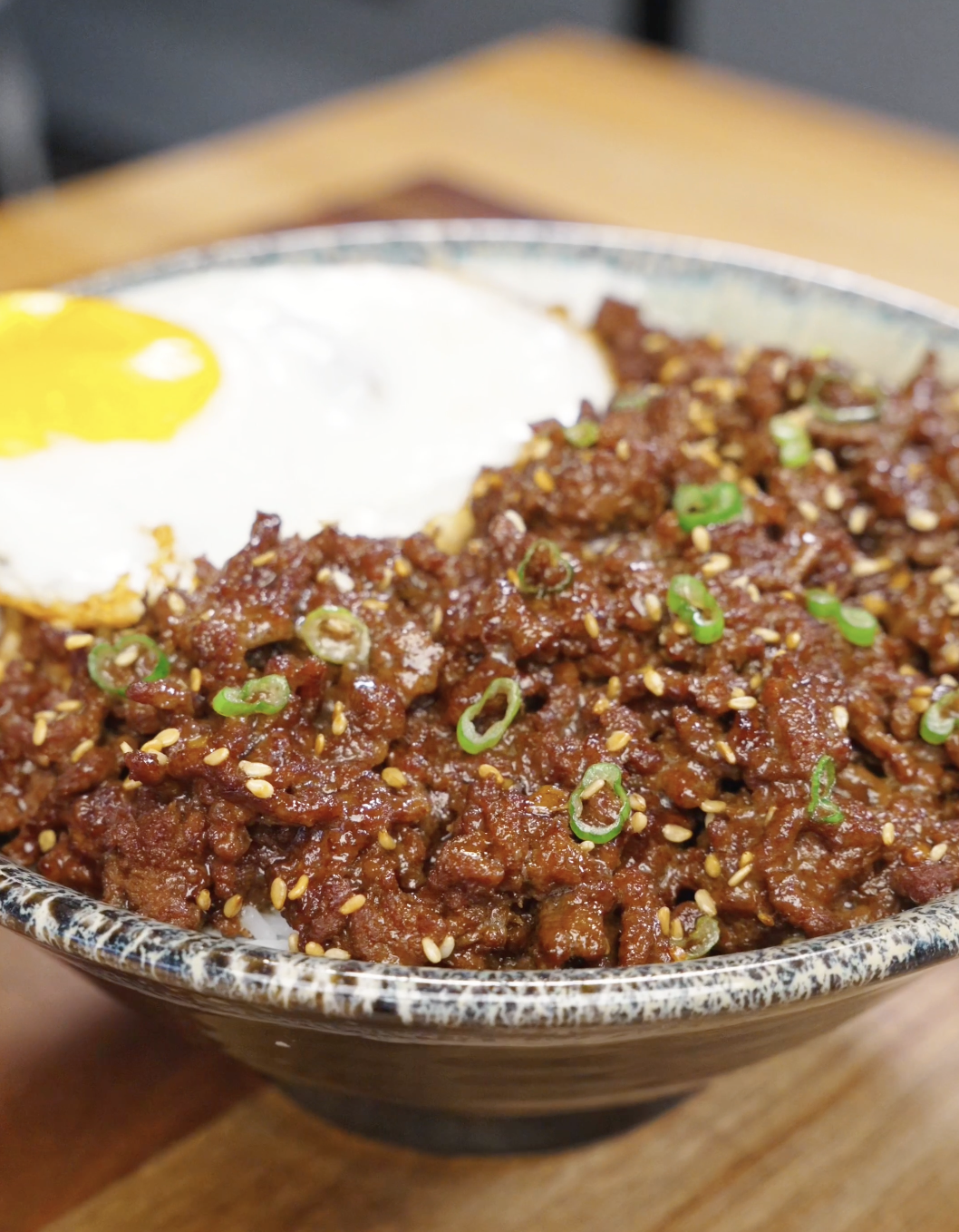 Bowl of bulgogi ground beef served over rice with sesame seeds scallions and a fried egg.