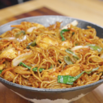 Chicken chow mein served in a bowl with stir-fried noodles, tender chicken, cabbage, carrots, and scallions coated in a glossy soy-based sauce.