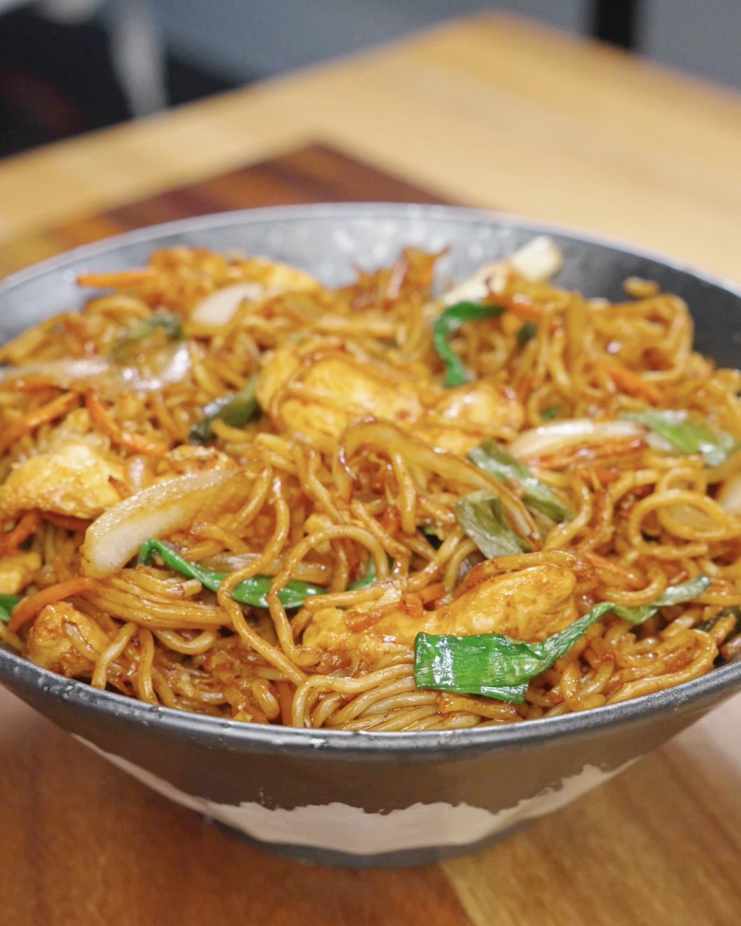 Chicken chow mein served in a bowl with stir-fried noodles, tender chicken, cabbage, carrots, and scallions coated in a glossy soy-based sauce.