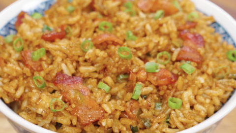 Bowl of garlic bacon fried rice topped with crispy bacon pieces and fresh scallions.