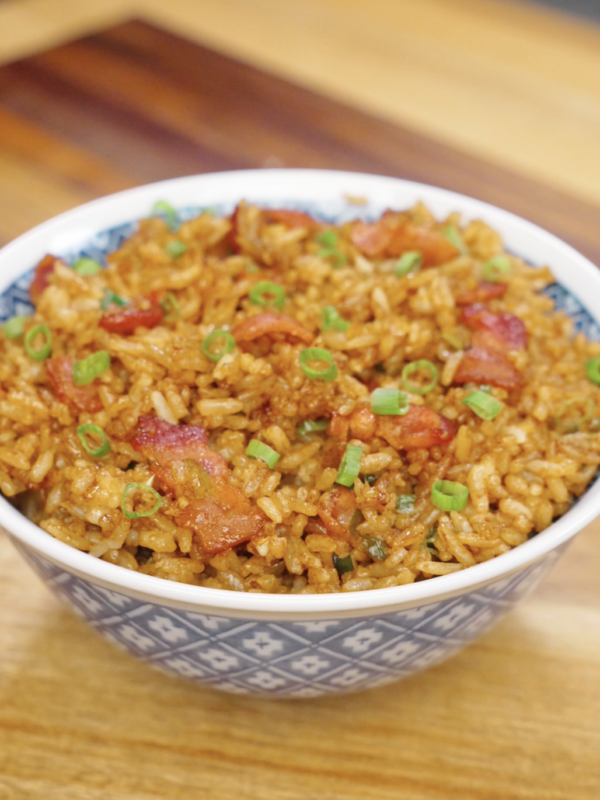 Bowl of garlic bacon fried rice topped with crispy bacon pieces and fresh scallions.