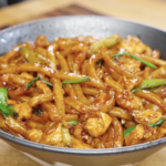 Bowl of garlic chicken noodles coated in a glossy soy-based sauce with chicken and scallions.