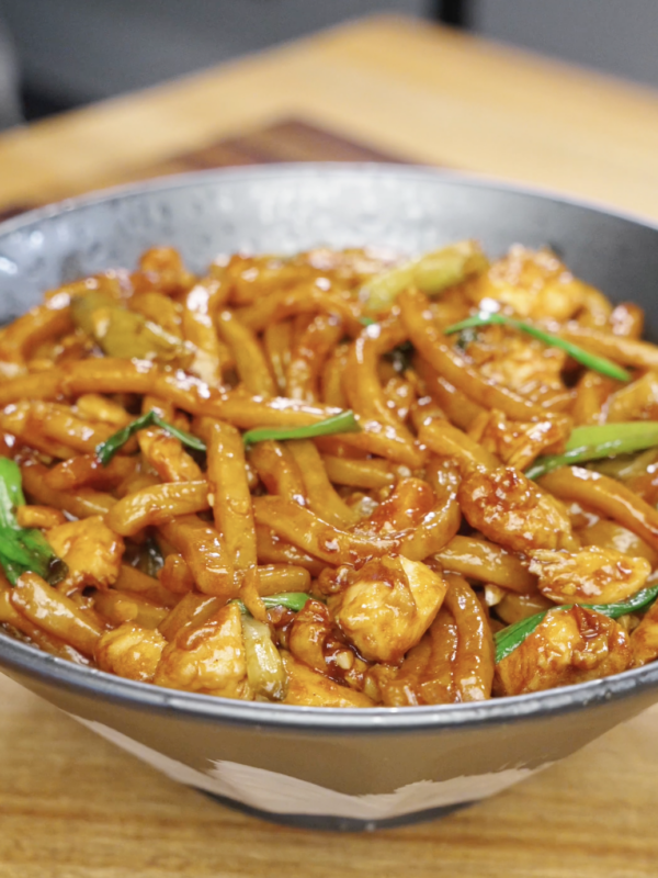 Bowl of garlic chicken noodles coated in a glossy soy-based sauce with chicken and scallions.