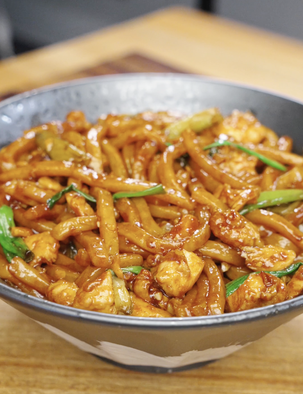 Bowl of garlic chicken noodles coated in a glossy soy-based sauce with chicken and scallions.