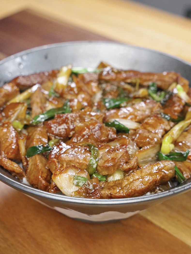 Bowl of Mongolian beef stir fry with tender beef slices, saut&eacute;ed onions, and scallions coated in a rich, glossy sauce from this Mongolian Beef Recipe.
