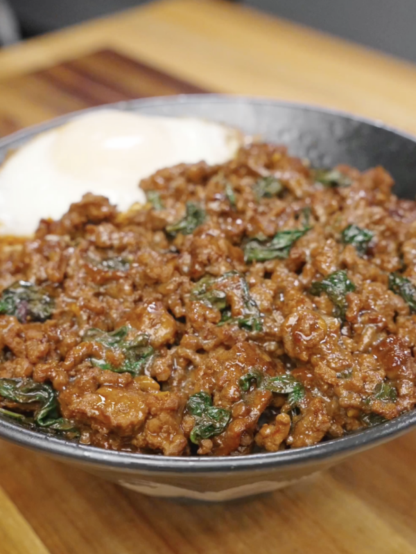Thai basil ground beef served over white rice with a fried egg, showcasing a rich, glossy sauce and fresh basil.
