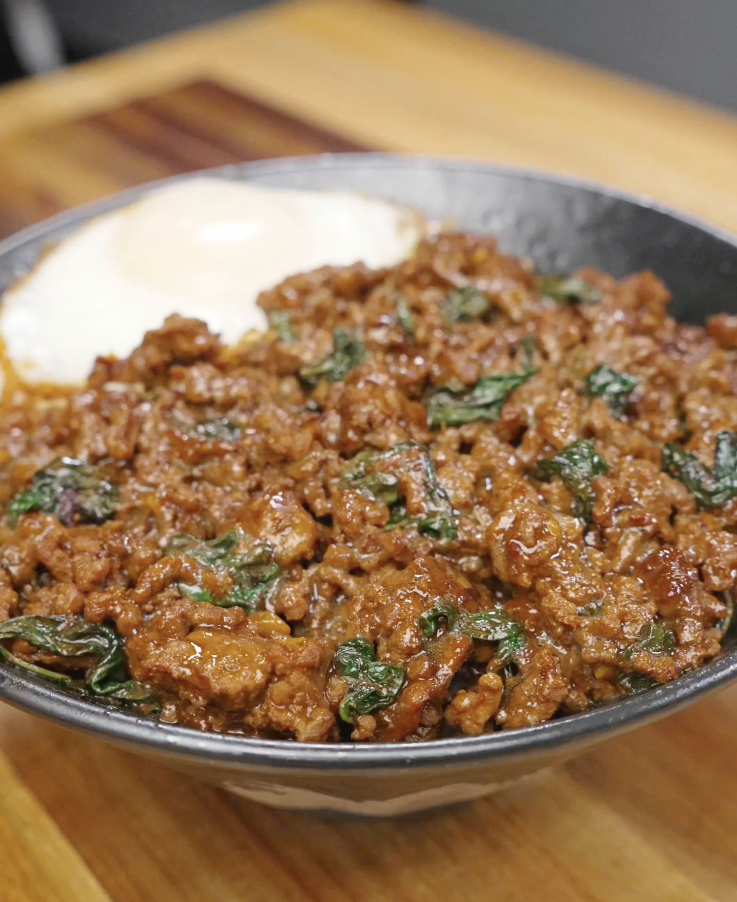 Thai basil ground beef served over white rice with a fried egg, showcasing a rich, glossy sauce and fresh basil.