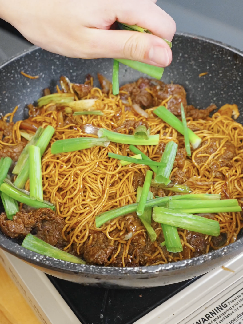 Fresh scallion greens being added to noodles and beef at the end of cooking in the Beef Chow Mein Recipe.