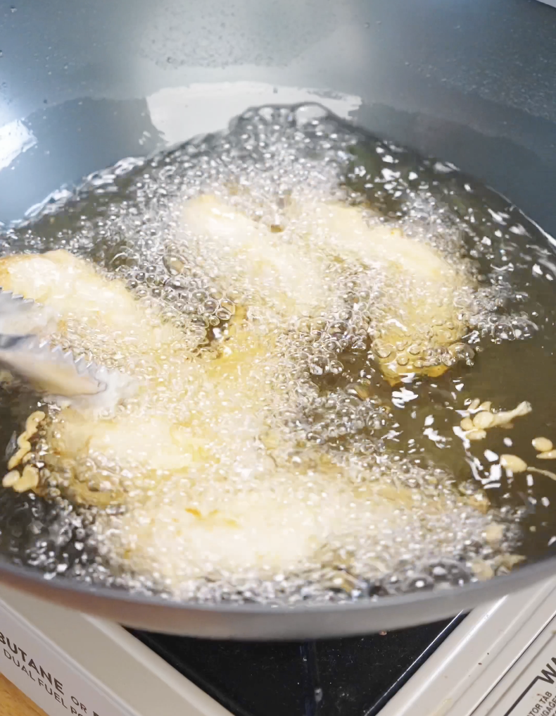 Chicken tenders frying in hot oil, bubbling intensely as the batter crisps up for the Honey Butter Chicken Tenders Recipe.