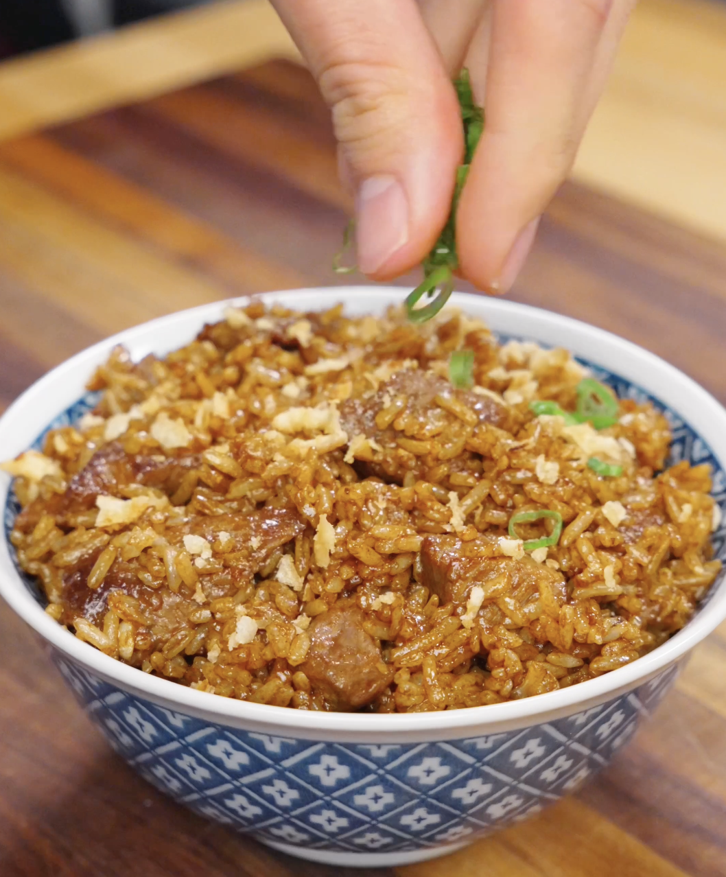 Fresh sliced scallions being sprinkled over garlic beef fried rice in a bowl, adding color, freshness, and contrast to the rich savory dish.