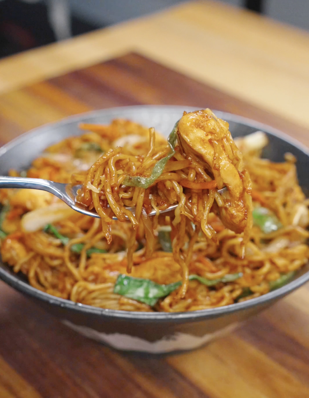 Chopsticks lifting saucy chicken chow mein noodles with vegetables, showing the texture and glossy coating of the stir fry.