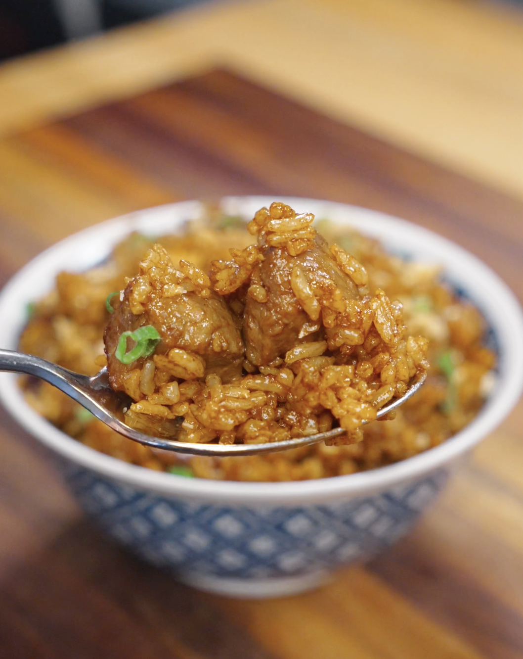 A spoonful of garlic beef fried rice being lifted, showing tender beef cubes and glossy soy-coated rice grains with a rich, savory finish.