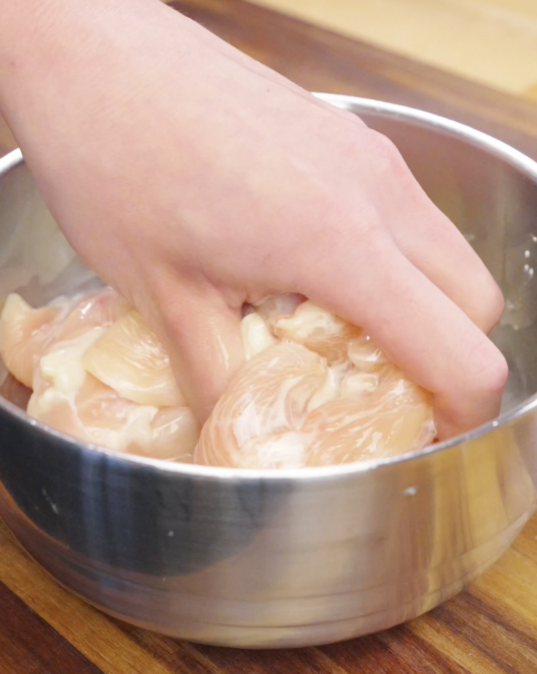 Sliced chicken breast being mixed with marinade in a bowl, preparing the protein for chicken chow mein stir fry.