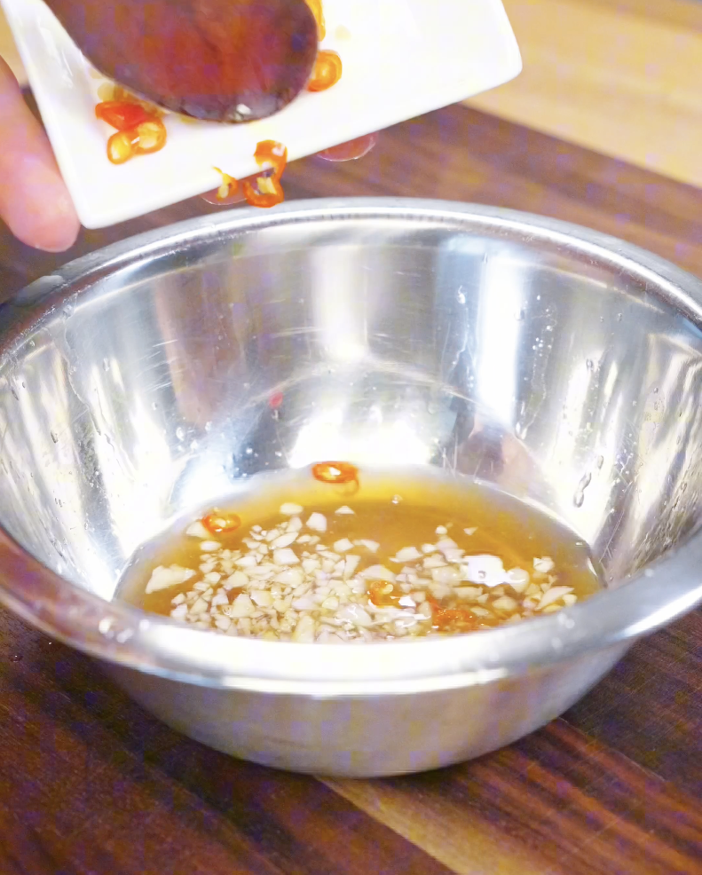 Garlic and sliced Thai chilies being added into a bowl with fish sauce and lime juice to create the tangy dressing for the Vietnamese Crispy Pork Belly Recipe.