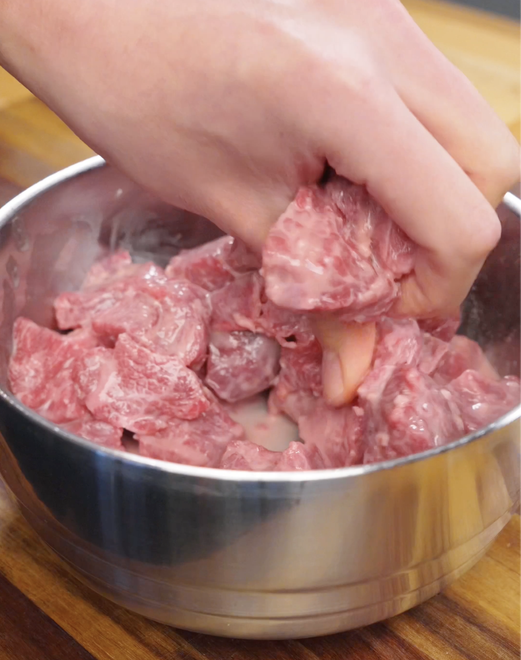 Cubed beef being mixed with Shaoxing wine, salt, and cornstarch in a bowl to tenderize and prepare it for searing in garlic beef fried rice.