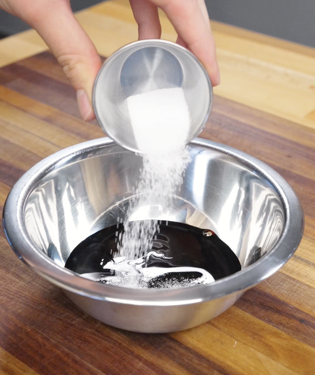 Sugar being added to soy sauce mixture in a bowl for garlic chicken noodles sauce.