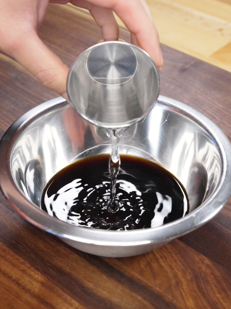 Clear liquid being poured into soy sauce in a metal bowl to create the savory-sweet sauce base for the Mongolian Beef Recipe.