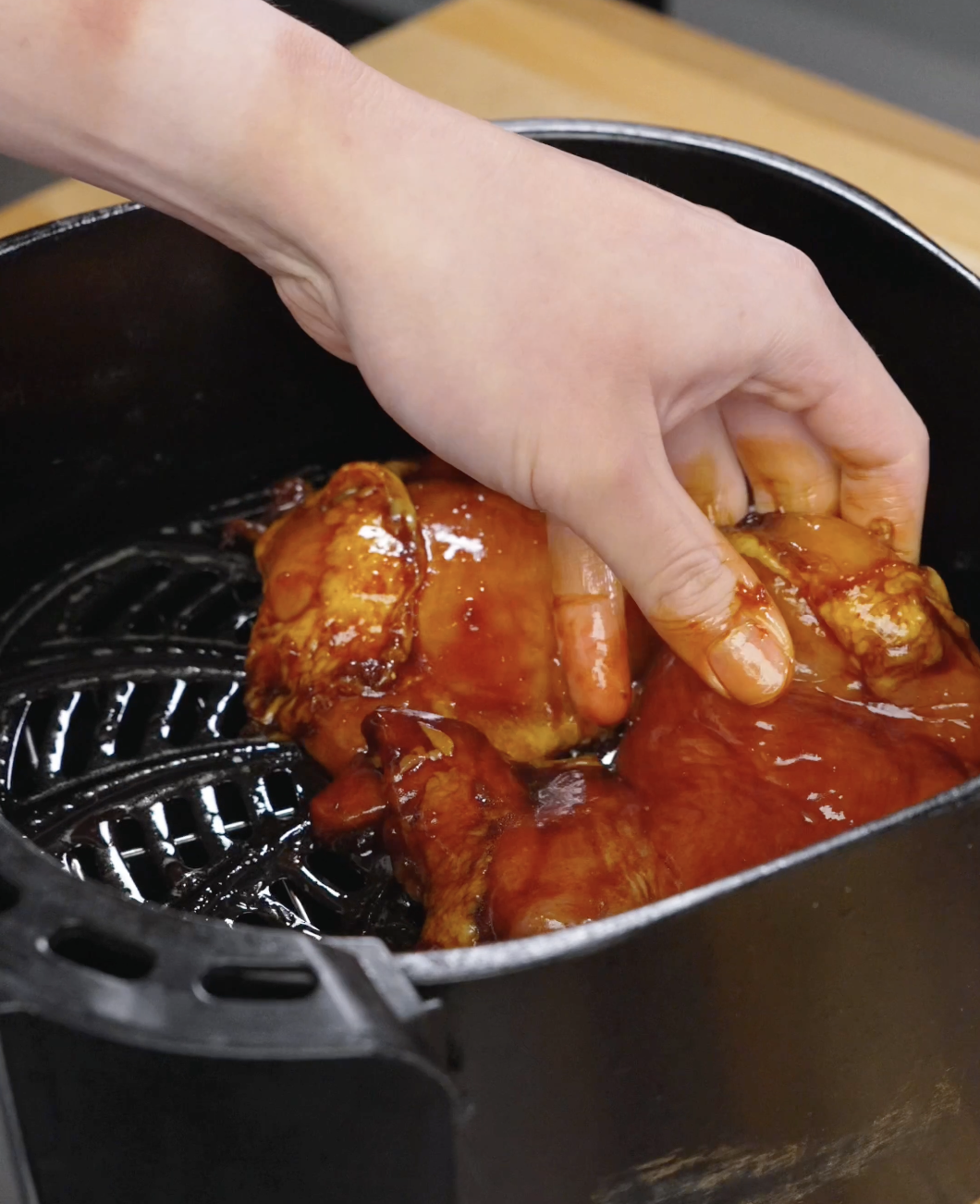 Marinated chicken thighs being placed into an air fryer basket, coated in a rich bulgogi sauce ready to cook until caramelized and juicy.