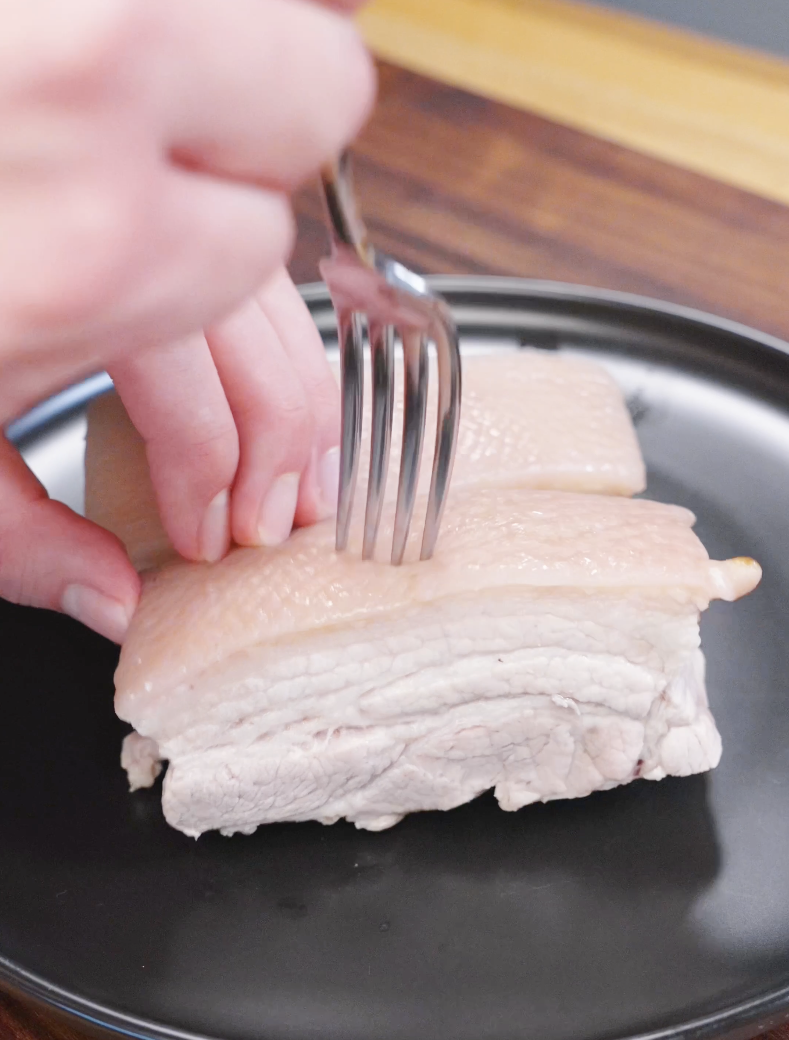 Close-up of a fork poking holes into boiled pork belly skin to help achieve crispy crackling in the Vietnamese Crispy Pork Belly Recipe.