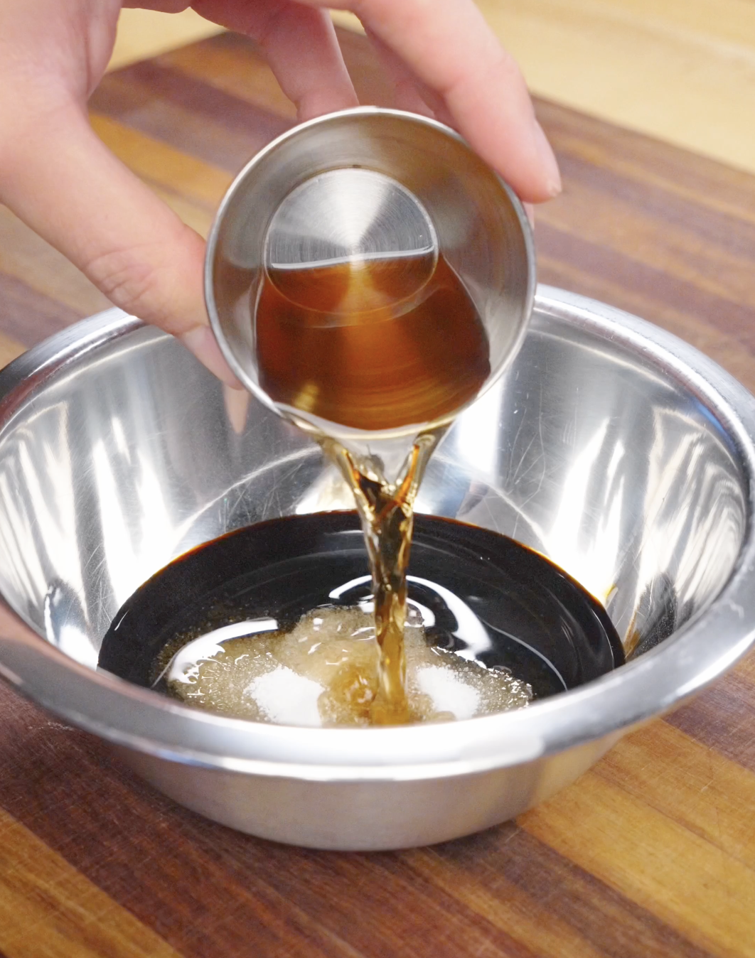 Soy-based chow mein sauce being poured into a mixing bowl with sugar and seasonings, preparing the stir fry sauce.