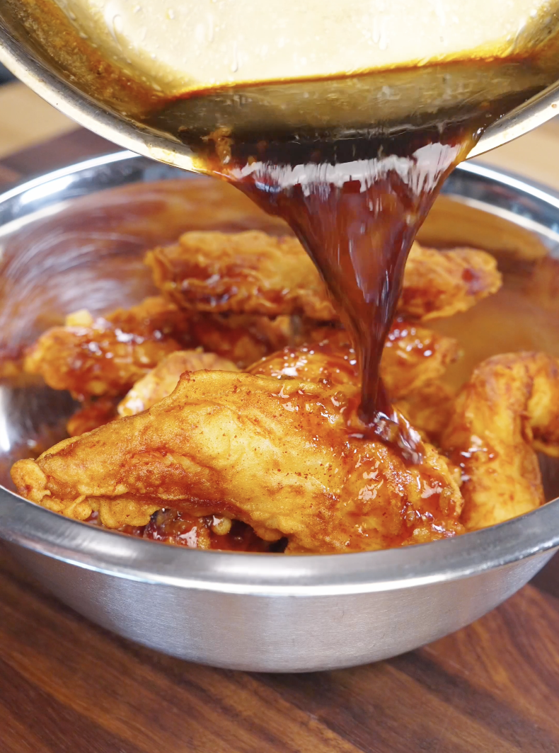 Thick honey butter sauce being poured over crispy fried chicken in a bowl, coating each piece evenly.
