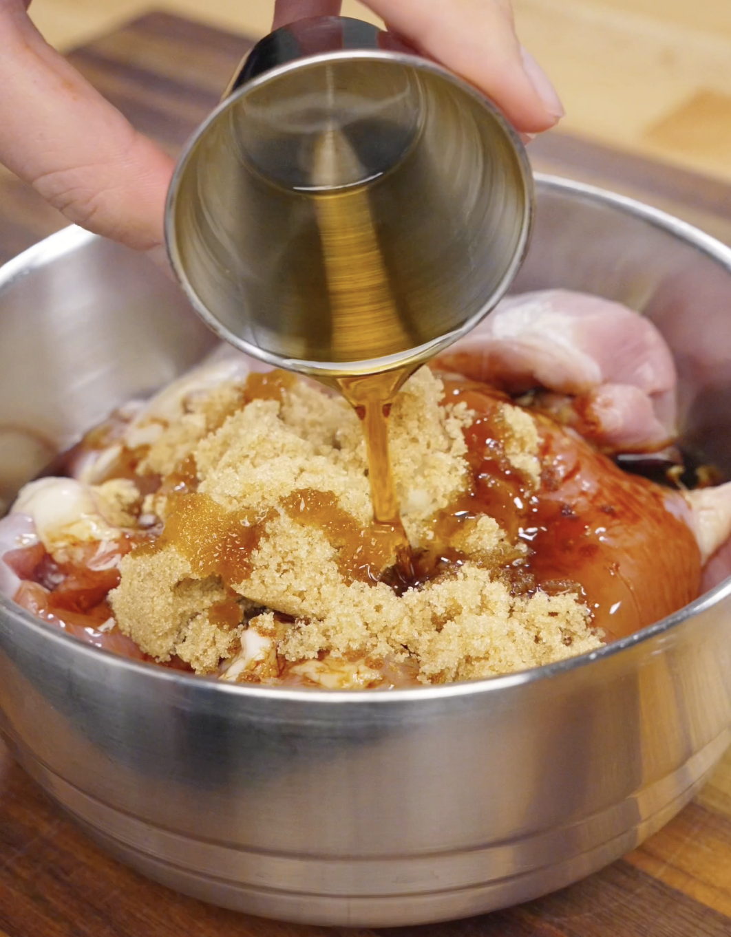 Honey being poured over chicken thighs in a bowl with soy sauce, gochujang, garlic, and brown sugar to create a sweet and savory Korean bulgogi marinade.